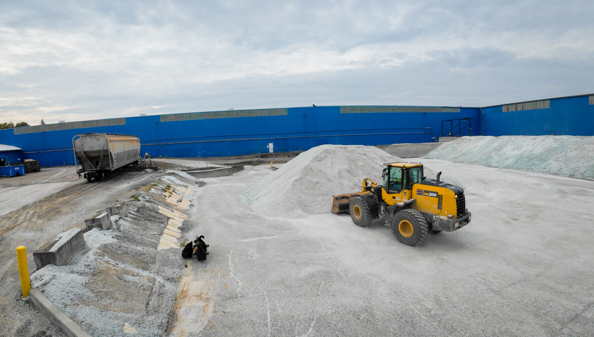 Front loader moving piles of recycled glass cullet in the yard outside an Anchor Glass plant